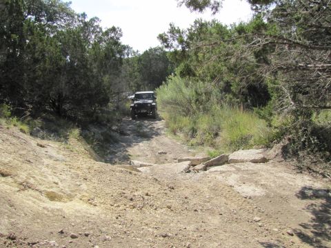 1995 Ford Bronco - An off-road vehicle navigates a challenging dirt trail surrounded by dense vegetation.