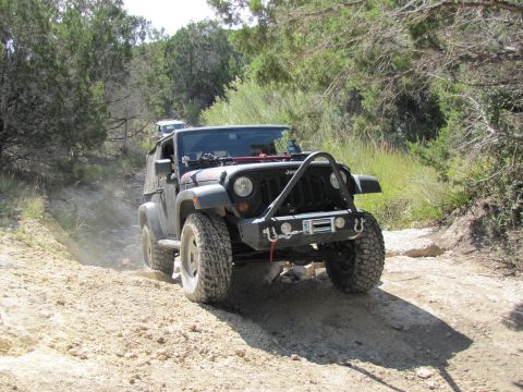 1995 Ford Bronco - A black Jeep Wrangler navigates a dusty off-road trail, with another vehicle following in the distance.