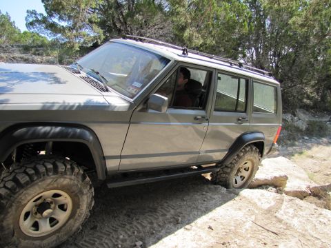 1995 Ford Bronco - A Jeep Cherokee XJ navigates a challenging off-road path with large tires and a lifted suspension.