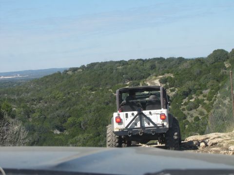 1995 Ford Bronco - A white Jeep Wrangler navigates a dirt path through a wooded, hilly landscape.