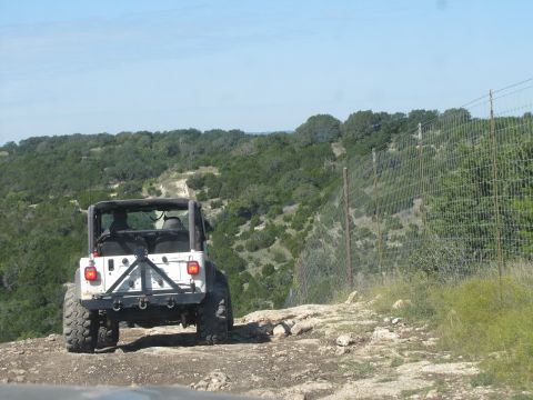1995 Ford Bronco - Jeep Wrangler navigates a rough, off-road trail with a scenic, hilly landscape.