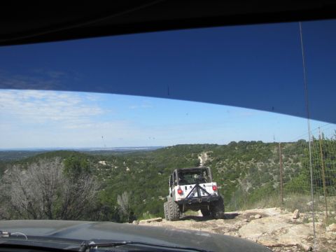 1995 Ford Bronco - A white Jeep is parked on a dirt path overlooking a vast, green, hilly landscape under a clear blue sky.