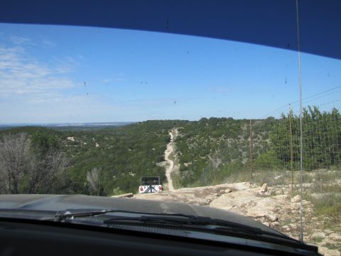 1995 Ford Bronco - A white SUV navigates a winding dirt road through a scenic, hilly terrain under a clear blue sky.