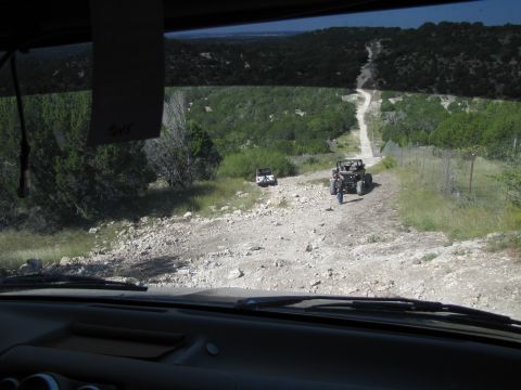 1995 Ford Bronco - Two off-road vehicles navigate a dirt path through a rural, wooded landscape.