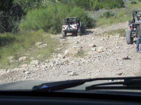 1995 Ford Bronco - Two Jeep Wranglers navigate a rough, rocky trail surrounded by dry brush and sparse vegetation.