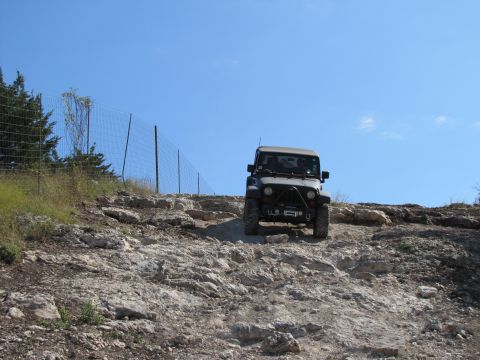 1995 Ford Bronco - A Jeep Wrangler navigates a challenging rocky terrain under a clear blue sky.