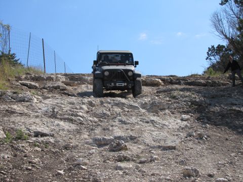 1995 Ford Bronco - A Jeep Wrangler navigates a steep, rocky incline under a clear blue sky.