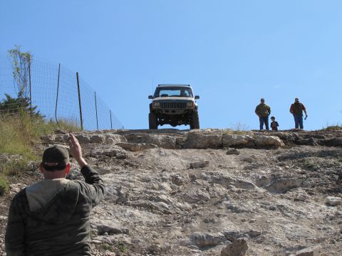 1995 Ford Bronco - White Jeep Cherokee navigates a challenging rocky terrain under a clear blue sky.