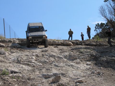 1995 Ford Bronco - A Jeep Cherokee XJ navigates a challenging rocky incline while onlookers observe the off-road adventure.