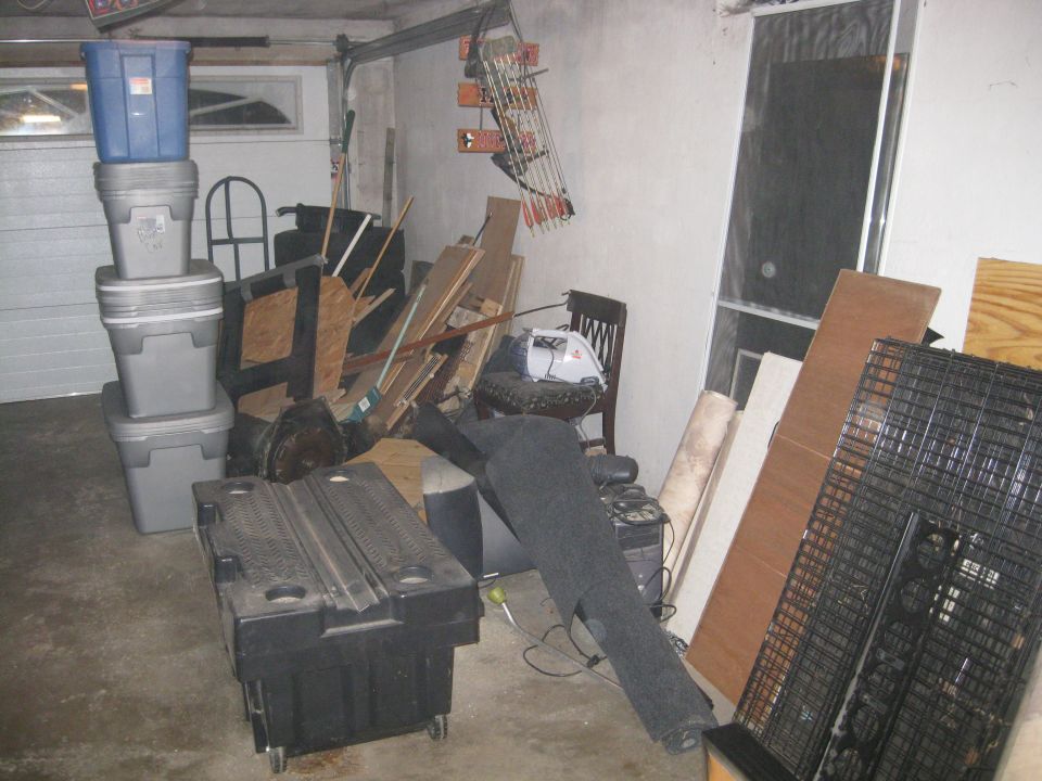 Garage interior with stacked storage bins, lumber leaning against a wall, and a bow and arrows mounted on the wall