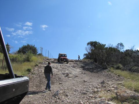 1995 Ford Bronco - Two off-road vehicles navigate a steep, rocky incline under a clear blue sky.