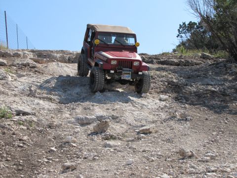 1995 Ford Bronco - A red Jeep Wrangler navigates a steep, rocky incline under a clear blue sky.