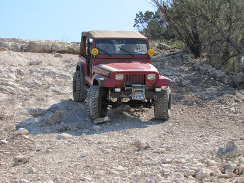 1995 Ford Bronco - This red Jeep Wrangler navigates a rocky incline, its front end clearly visible with distinctive smiley face headlights.
