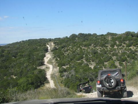 1995 Ford Bronco - Two Jeeps navigate a challenging dirt path through a dense, green landscape under a clear blue sky.