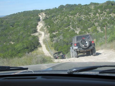 1995 Ford Bronco - Two Jeep Wranglers navigate a challenging dirt path through a dry, scrubby landscape under a clear blue sky.