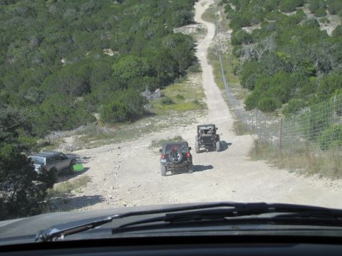 1995 Ford Bronco - Multiple Jeeps navigate a dusty, off-road path through a dry, scrubby landscape.