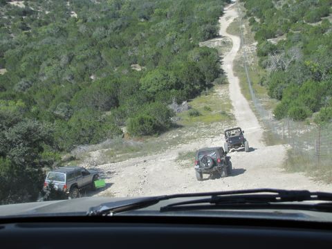 1995 Ford Bronco - Multiple Jeeps navigate a winding dirt road in a rural, wooded landscape.