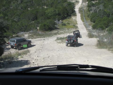 1995 Ford Bronco - Multiple off-road vehicles navigate a dusty trail through a rural, wooded landscape.