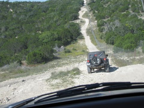 1995 Ford Bronco - Two vehicles navigate a steep, unpaved road through a landscape of trees and brush.