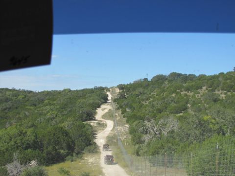 1995 Ford Bronco - Two SUVs navigate a dusty, winding road through a dense, green landscape under a clear blue sky.