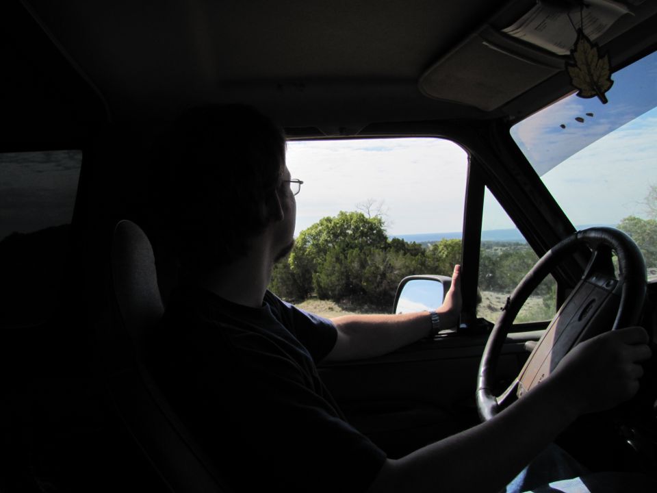 Person driving a vehicle, looking out the passenger window at a landscape. Steering wheel and dashboard visible
