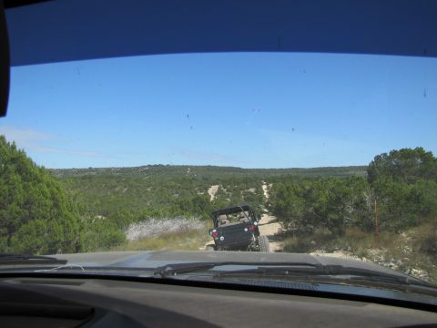 1995 Ford Bronco - Two vehicles navigate a dusty trail through a wooded, hilly landscape under a clear blue sky.