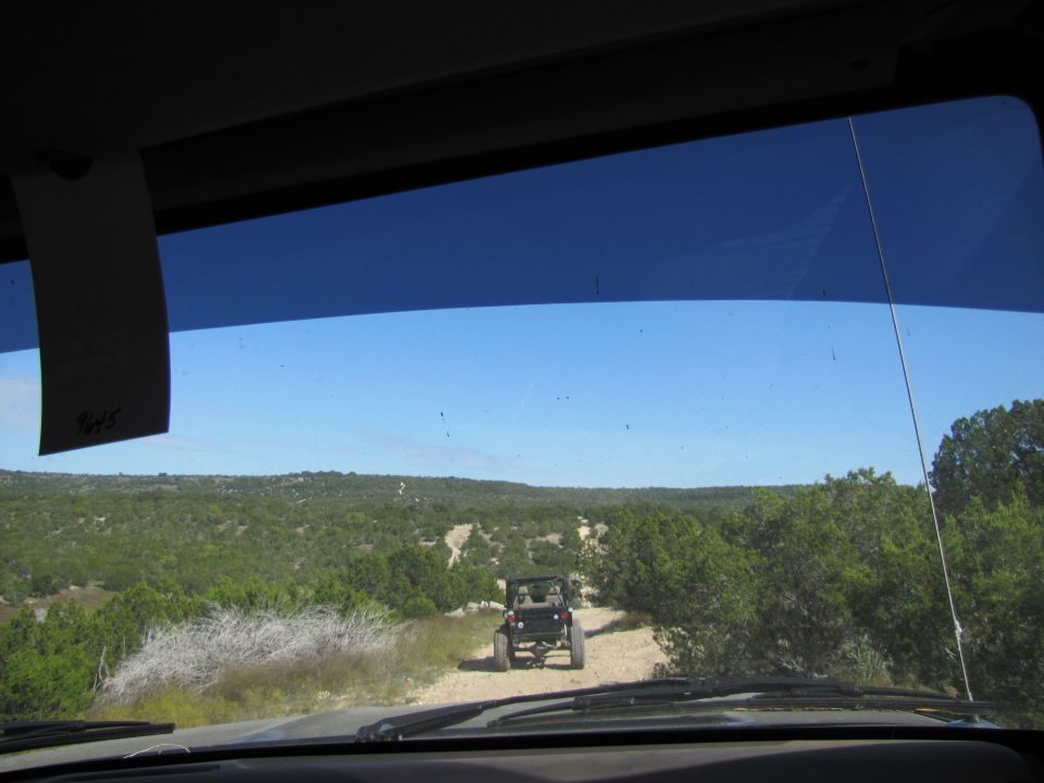 View from inside a vehicle looking at another off-road vehicle on a dirt path through a wooded landscape