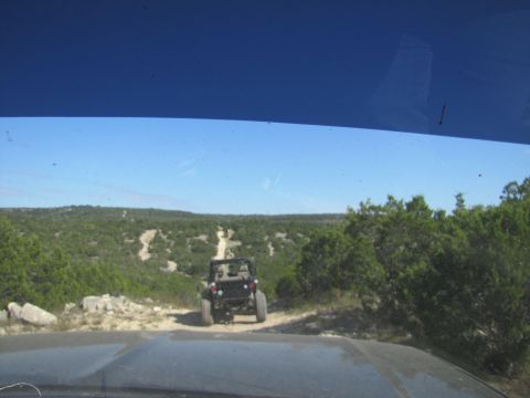 1995 Ford Bronco - Two vehicles on a dirt road in a scenic, wooded landscape under a clear blue sky.