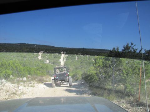 1995 Ford Bronco - Two off-road vehicles navigate a dusty trail through a dry, scrubby landscape under a clear blue sky.