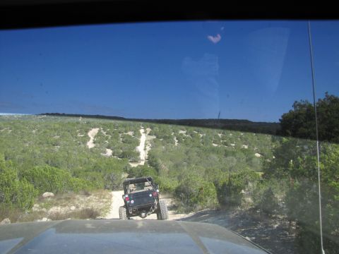1995 Ford Bronco - Jeep navigates an off-road trail in a dry, brush-covered terrain.