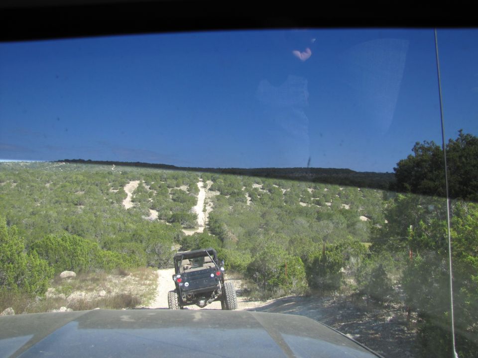 Jeep driving on a dirt trail through a hilly, scrubby landscape under a clear blue sky