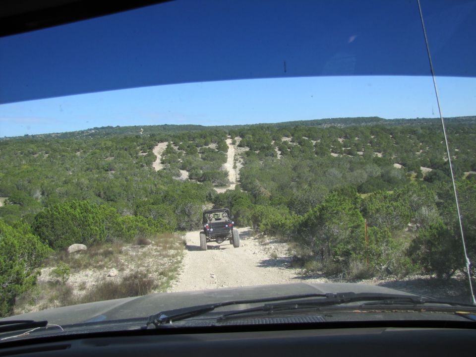 Two off-road vehicles driving on a dirt path through a wooded, hilly landscape