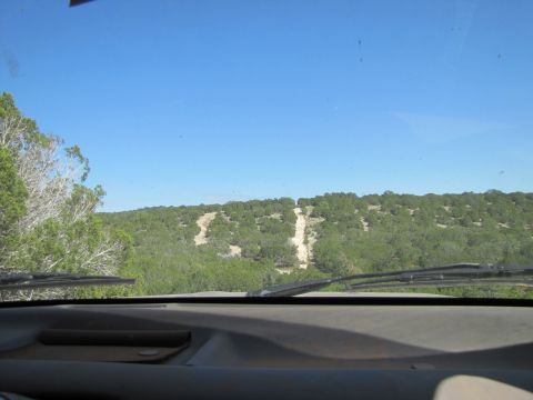 1995 Ford Bronco - View from inside a vehicle on a dirt road, with a wooded hillside ahead.