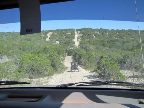 1995 Ford Bronco - Two off-road vehicles travel down a dusty trail through a wooded, hilly landscape.