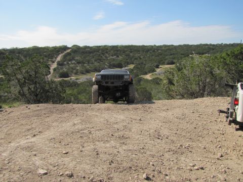 1995 Ford Bronco - A modified Jeep Cherokee XJ is seen from the front on a dirt trail with a second vehicle partially visible to the right.