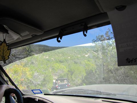 1995 Ford Bronco - Driving on a dirt road with another vehicle ahead, surrounded by trees and hills.