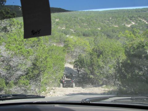 1995 Ford Bronco - A red Jeep Wrangler navigates a dirt path through a wooded, hilly landscape.