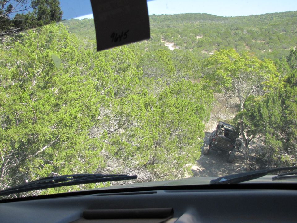 View from inside a vehicle looking out at an off-road vehicle navigating a steep, wooded trail