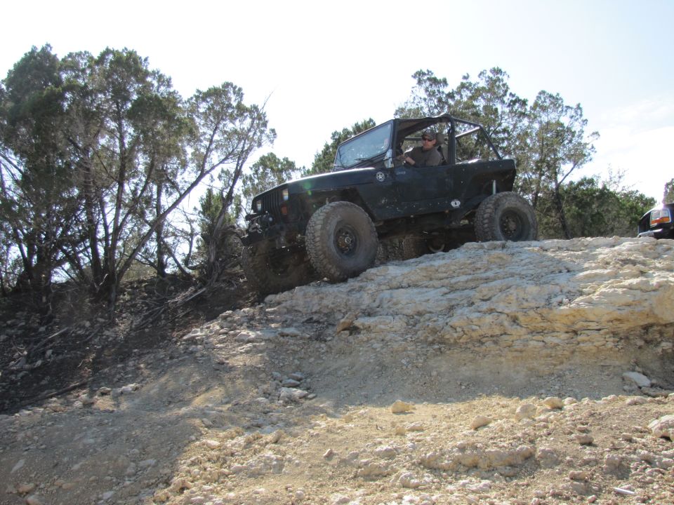 Black Jeep Wrangler climbing a rocky incline, front passenger side tire visible, driver visible