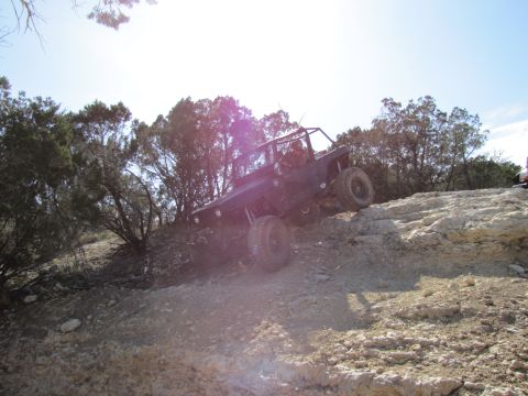 1995 Ford Bronco - A modified off-road vehicle navigates a steep, rocky terrain under a bright sky.