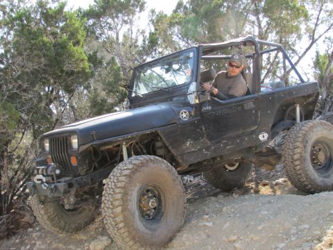1995 Ford Bronco - A black Jeep Wrangler Renegade navigates a challenging off-road course with large tires and a roll cage.