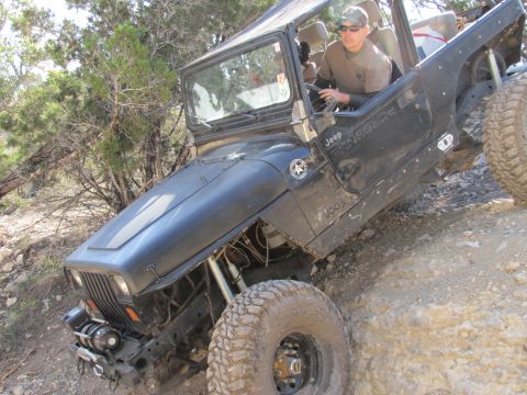 1995 Ford Bronco - Man driving a black Jeep Wrangler off-road on a steep, rocky trail.