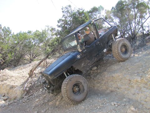 1995 Ford Bronco - A black Jeep Wrangler navigates a steep, rocky trail with a driver at the wheel.