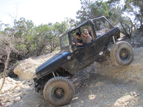 1995 Ford Bronco - A black Jeep Wrangler navigates a steep, rocky incline with two occupants inside.