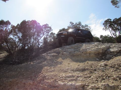 1995 Ford Bronco - A black SUV navigates a rocky trail under a bright, partly cloudy sky.