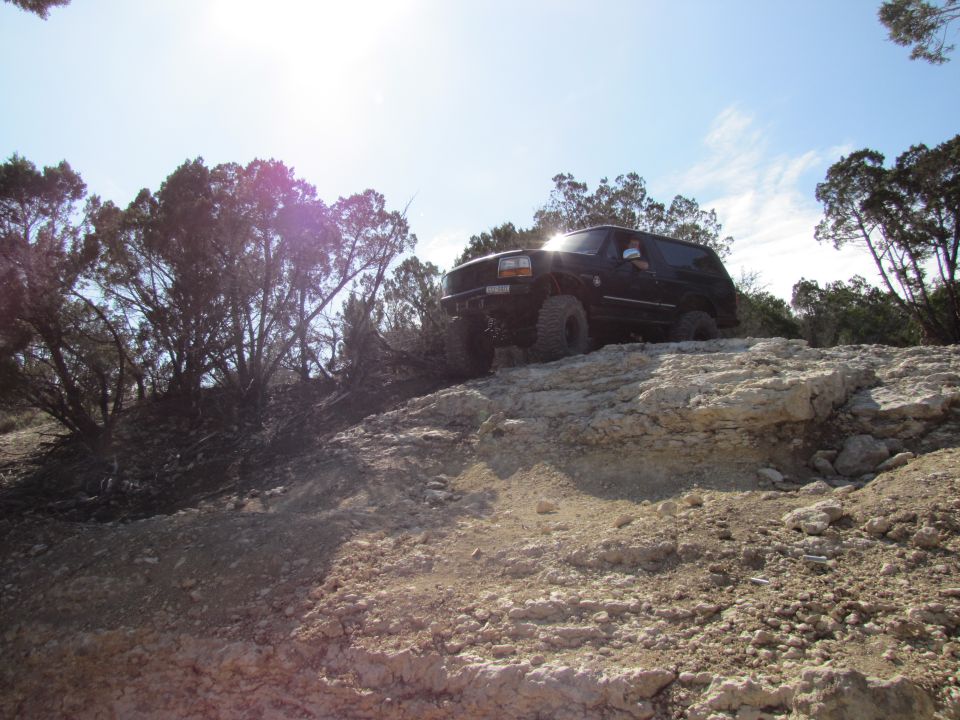 Black SUV climbing rocky terrain with trees and blue sky