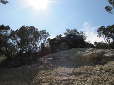 1995 Ford Bronco - A black 1995 Ford Bronco navigates a , rocky landscape on a clear day.