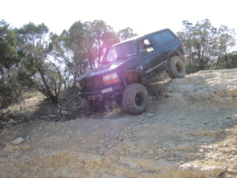 1995 Ford Bronco - A black Ford Bronco navigates a challenging off-road trail with steep inclines and rocky terrain.