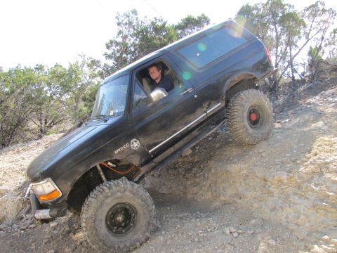 1995 Ford Bronco - A black Ford Bronco navigates a steep, rocky trail with its driver behind the wheel.