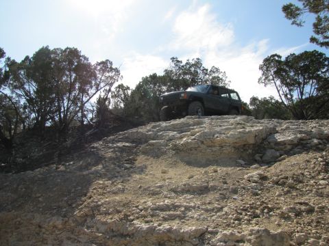 1995 Ford Bronco - A Jeep Cherokee XJ navigates a rocky incline under a partly cloudy sky.